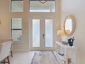 A modern entryway with a white door, a bench, a console table with a lamp, and a mirror. - 5 Bedroom, Saltwater Heated Pool & Spa, Dock: The Coastal Cabana (Cape Coral)