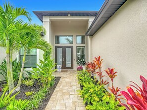 A modern house with a paved entrance, a welcome sign, and a variety of plants. - 5 Bedroom, Saltwater Heated Pool & Spa, Dock: The Coastal Cabana (Cape Coral)