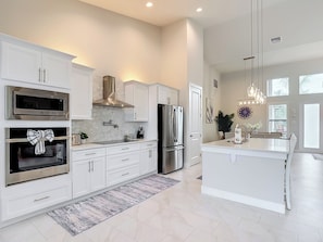 A modern kitchen with white cabinetry, stainless steel appliances, and a large island. - 5 Bedroom, Saltwater Heated Pool & Spa, Dock: The Coastal Cabana (Cape Coral)