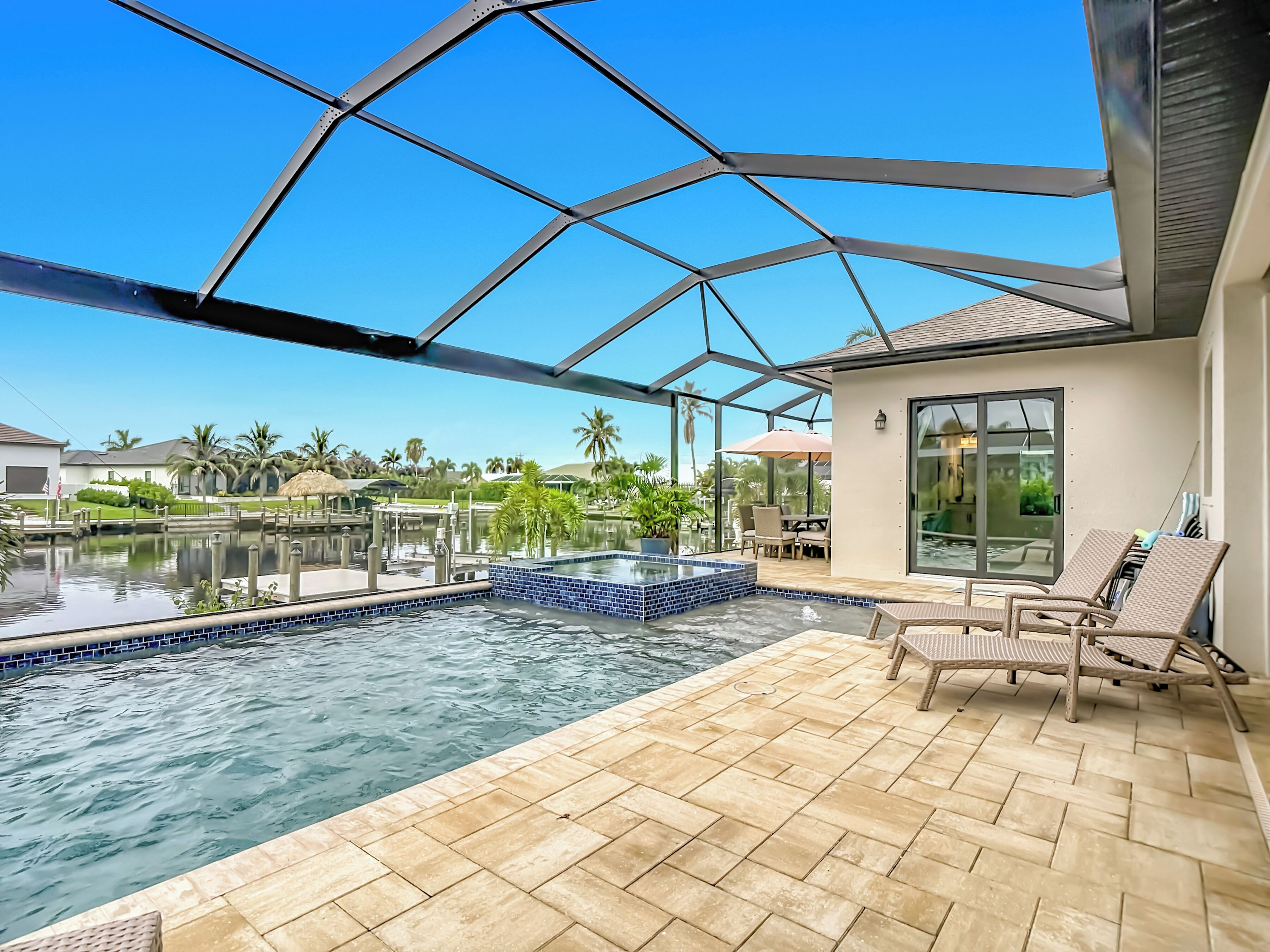 A pool area with a hot tub, lounge chairs, and a view of a residential neighborhood.