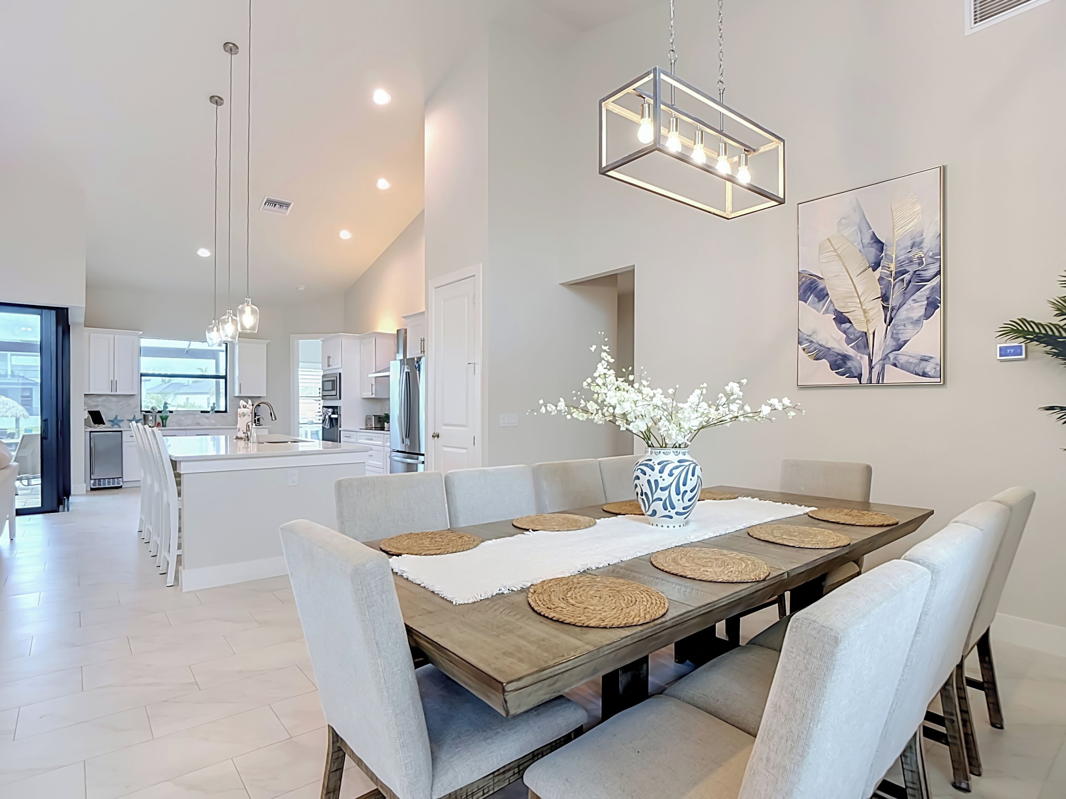 A modern kitchen with white cabinets, stainless steel appliances, and a dining area with a wooden table and grey upholstered chairs.