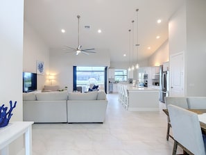 A modern living room with a sofa, TV, and a ceiling fan. - 5 Bedroom, Saltwater Heated Pool & Spa, Dock: The Coastal Cabana (Cape Coral)