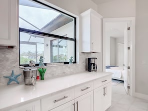 A modern kitchen with a large window, white cabinetry, and a coffee maker on the counter. - 5 Bedroom, Saltwater Heated Pool & Spa, Dock: The Coastal Cabana (Cape Coral)