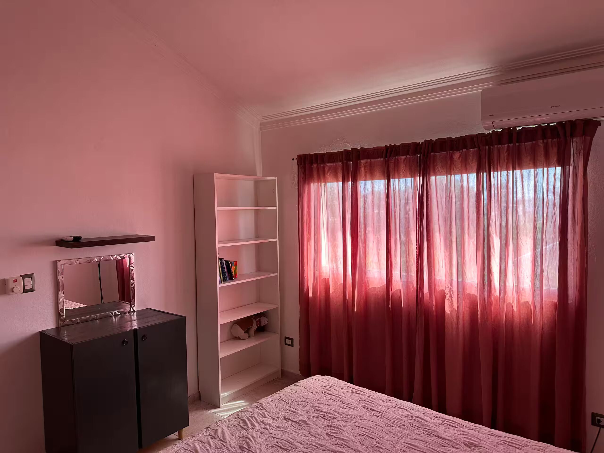 Un dormitorio con cama, armario, estantería y ventana con cortinas.