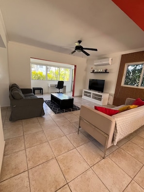 A living room with a sofa, a coffee table, a TV stand, and a ceiling fan. - 3BR Villa with Private Pool & Beach Access - Sleeps 6 (Punta Cana)