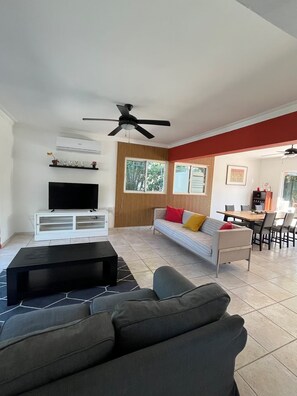 A modern living room with a flat-screen TV, a ceiling fan, a sofa, and a dining area with chairs. - 3BR Villa with Private Pool & Beach Access - Sleeps 6 (Punta Cana)