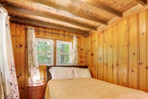 Une pièce en bois avec un lit, une table de chevet et une fenêtre avec des rideaux.