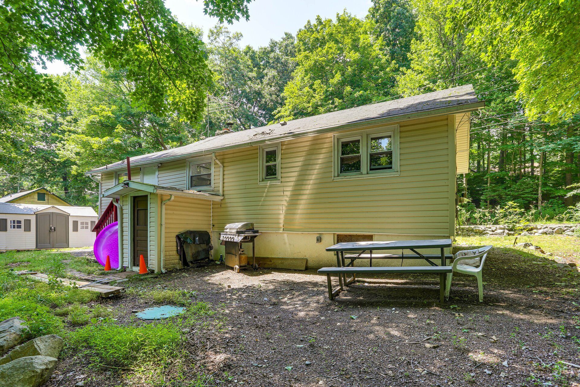 A single-story cabin with a porch, a grill, and a picnic table.