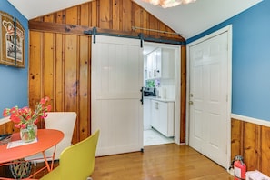 Une pièce avec un mur en bois, une porte blanche, une table rouge, une chaise jaune et un vase de fleurs.