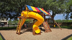 A playground with a yellow slide and climbing area. - Utopia Gruene Cottages (New Braunfels)