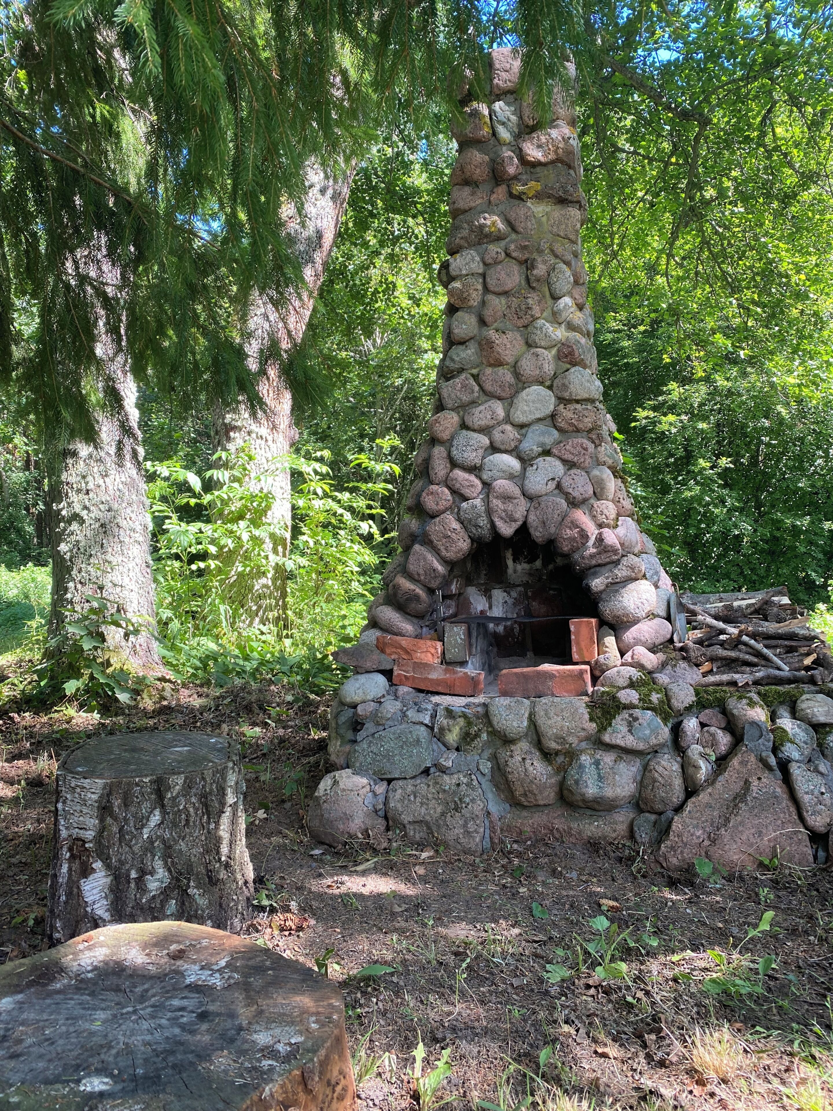A stone-built outdoor fireplace surrounded by trees.