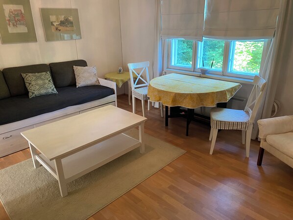 A living room with a sofa, a coffee table, a dining table with chairs, and a window with curtains.