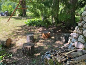 A natural outdoor area with a wooden swing, a pile of firewood, and a stone wall.