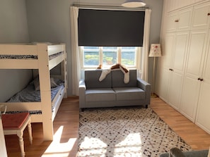 A room with bunk beds, a sofa, a patterned rug, and a window with a view.
