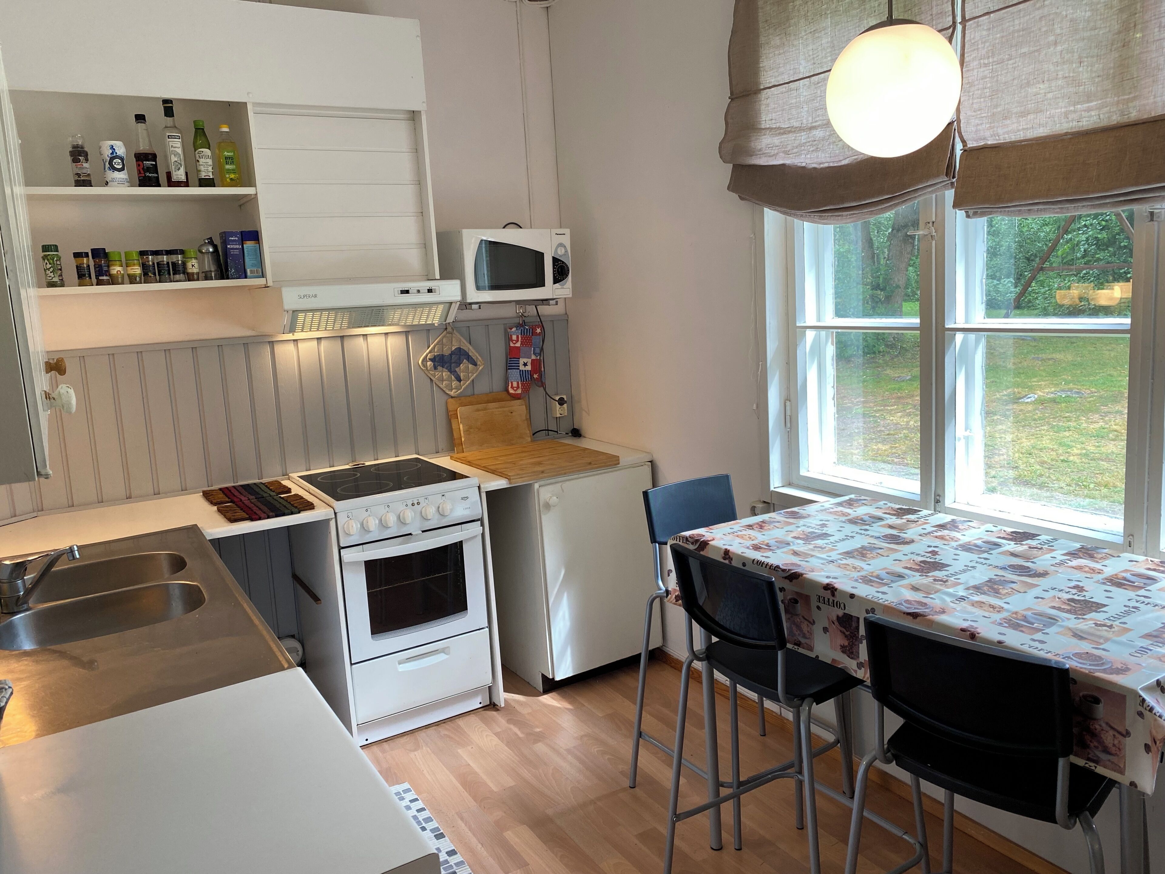 Une cuisine compacte équipée d’une cuisinière, d’un four à micro-ondes et d’un réfrigérateur, d’une table à manger avec des chaises et d’une fenêtre donnant sur un paysage verdoyant.