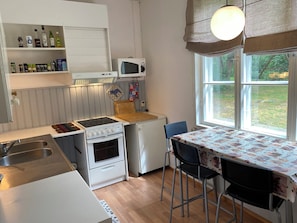 Une cuisine compacte équipée d’une cuisinière, d’un four à micro-ondes et d’un réfrigérateur, d’une table à manger avec des chaises et d’une fenêtre donnant sur un paysage verdoyant.