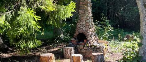 Ein aus Stein gemauerter Kamin im Freien, umgeben von Bäumen in einem bewaldeten Gebiet.