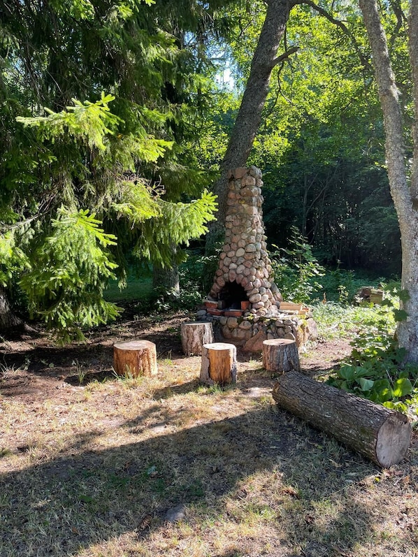 A stone-built outdoor fireplace surrounded by trees in a forested area.