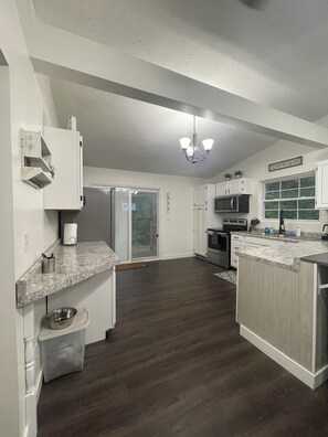 A spacious kitchen with a dark wood floor, white cabinetry, a built-in microwave, and a coffee bar sign.