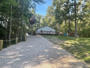 A gravel driveway leading to a wooden deck with a house in a wooded area.