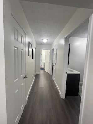 A hallway with white walls, dark wooden flooring, and white doors.