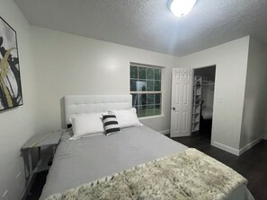 A bedroom with a bed, a window, a door, and a closet.