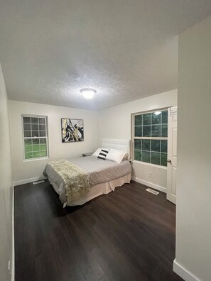 A bedroom with a bed, two windows, a ceiling light, and a door.