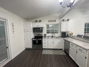 A kitchen with white cabinets, a microwave, an oven, a sink, and a coffee maker.