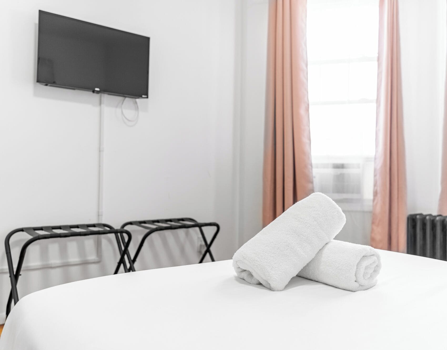 Habitación de hotel con cama, televisor montado en la pared y ventana con cortinas.