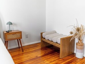 Ein Schlafzimmer mit einem Nachttisch aus Holz, einer Lampe, einer Bank mit Handtüchern und einer Vase mit Trockenpflanzen.