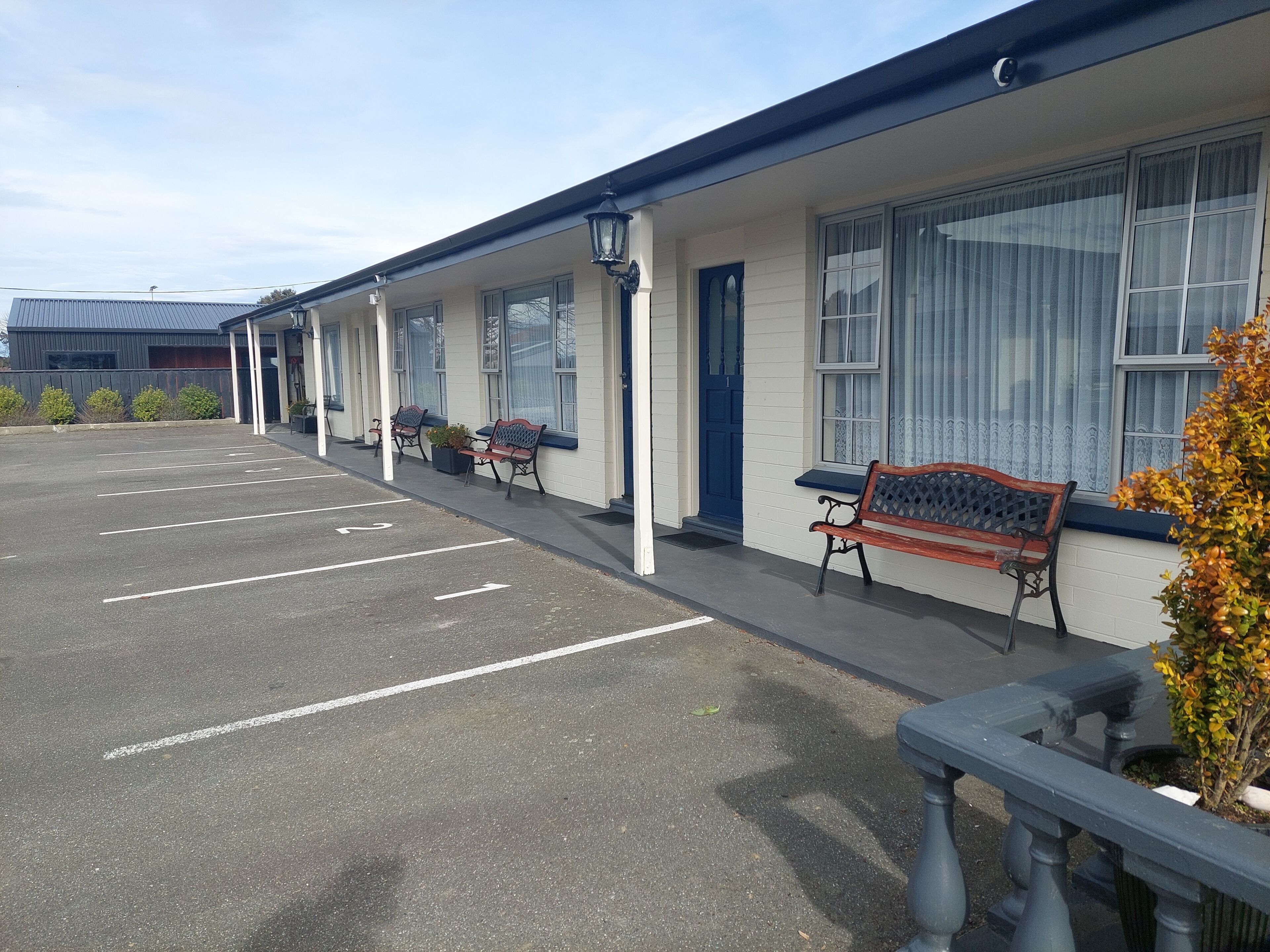 A motel with a parking lot, outdoor seating, and a building with large windows.