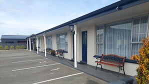 Un motel con estacionamiento, asientos al aire libre y un edificio con ventanas amplias.