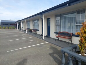 Un motel con estacionamiento, asientos al aire libre y un edificio con ventanas amplias.