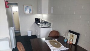 Una pequeña kitchenette con cafetera, un lavamanos y un armario. Hay una mesa con un mantel individual y un marco de fotos.