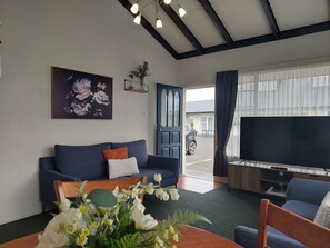 A living room with a sofa, a table with flowers, a TV, and a door leading outside. - Colonial On Tay Motel (Invercargill)