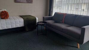 Una habitación con cama, sofá, una mesita y un cuadro en la pared, además de una ventana con cortinas.