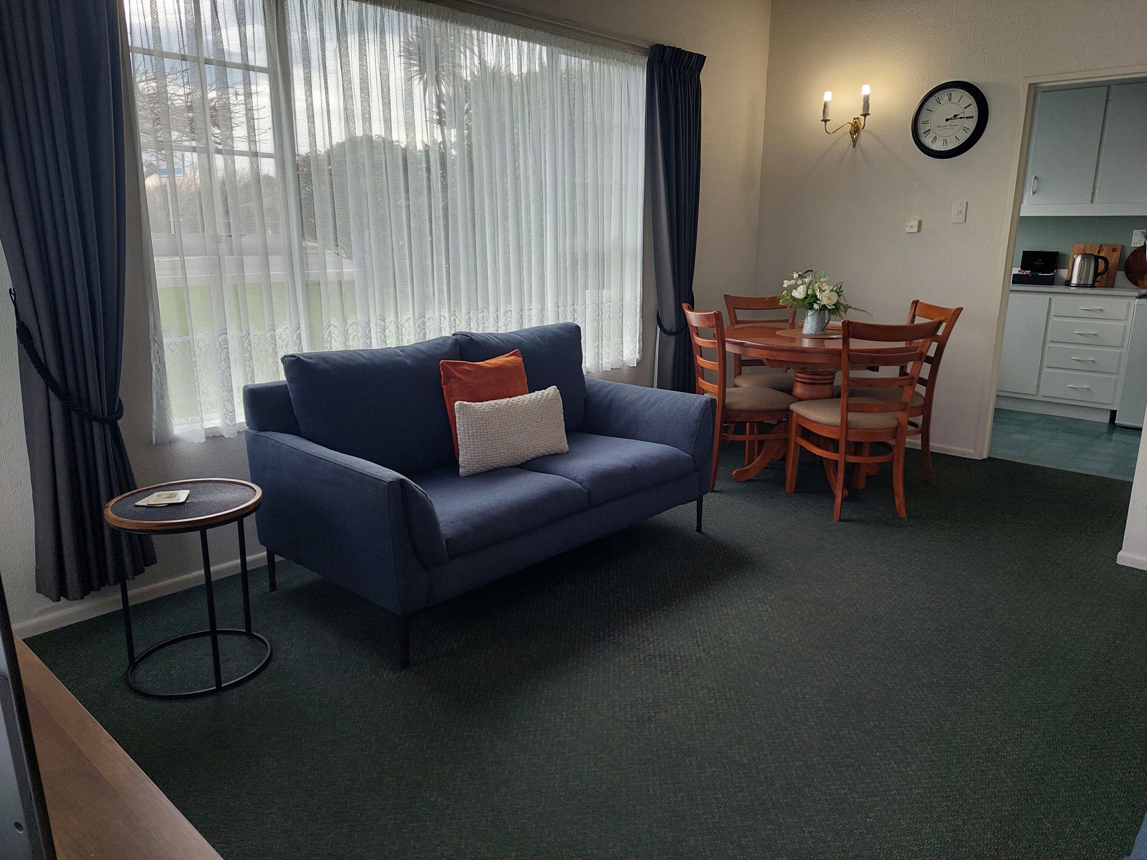 A living room with a blue sofa, a small round table, and a dining area with wooden chairs.