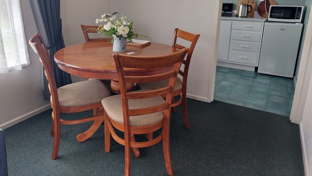 Comedor con una mesa redonda de madera, cuatro sillas, un jarrón con flores y un reloj en la pared.