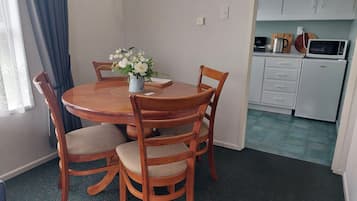 A dining area with a round wooden table, four chairs, a vase with flowers, and a clock on the wall.