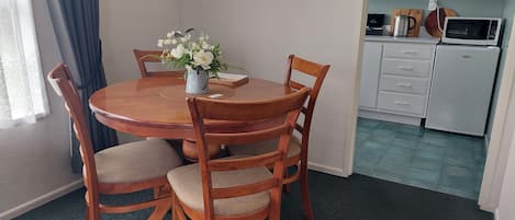Comedor con una mesa redonda de madera, cuatro sillas, un jarrón con flores y un reloj en la pared.