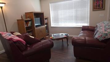 Ein Wohnzimmer mit zwei Ledersofas, einem Couchtisch, einem Bücherregal und einem Fenster mit Jalousien.