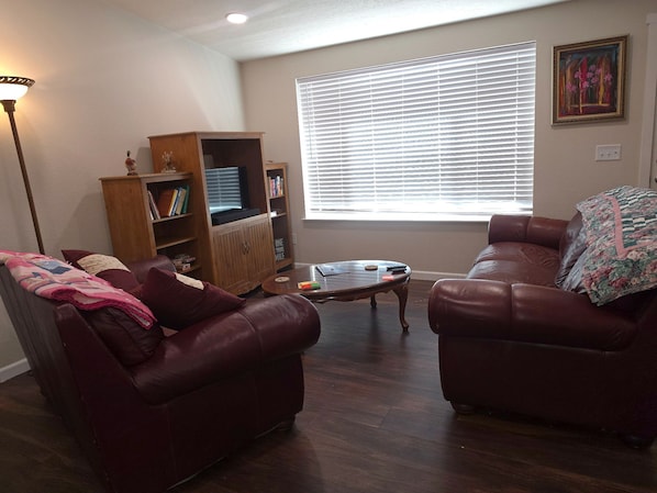 A living room with two leather sofas, a coffee table, a bookshelf, and a window with blinds.