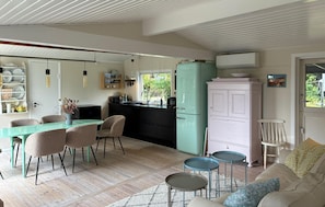 Een moderne keuken met een blauwgroene koelkast, een eethoek met een blauwgroene tafel en stoelen, en een zithoek met een bank en twee kleine bijzettafeltjes.