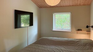 A bedroom with a bed, a wall-mounted TV, a window with a view of trees, and a ceiling light fixture. - 4 bedroom stunning home in Tisvildeleje (Tisvildeleje)