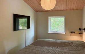 A bedroom with a bed, a wall-mounted TV, a window with a view of trees, and a ceiling light fixture. - 4 bedroom stunning home in Tisvildeleje (Tisvildeleje)