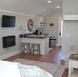A modern kitchen with a central island, bar stools, a flat-screen TV, and a microwave.