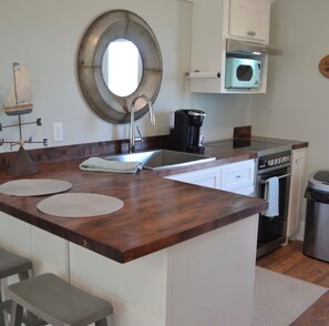 A kitchen with a wooden countertop, a sink, a stove, and a microwave.
