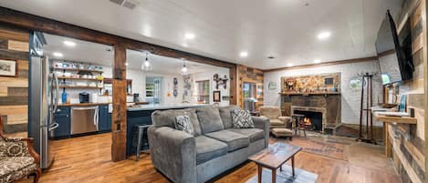 A spacious living area with a gray sofa, wooden flooring, and a fireplace.