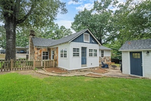 A small, single-story house with a stone chimney, a blue door, and a fenced yard.
