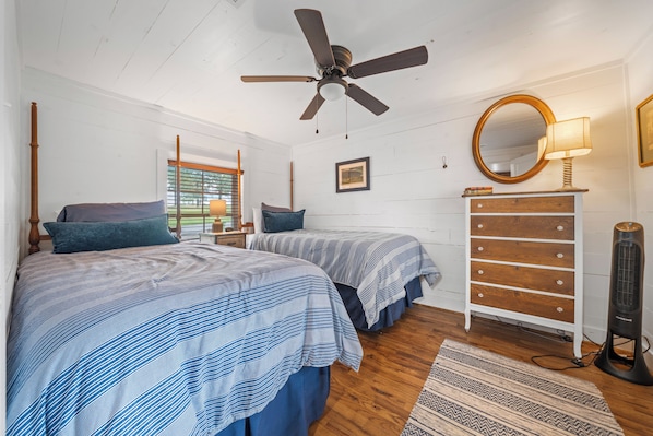 A bedroom with two beds, a ceiling fan, a dresser, a mirror, and a floor lamp.